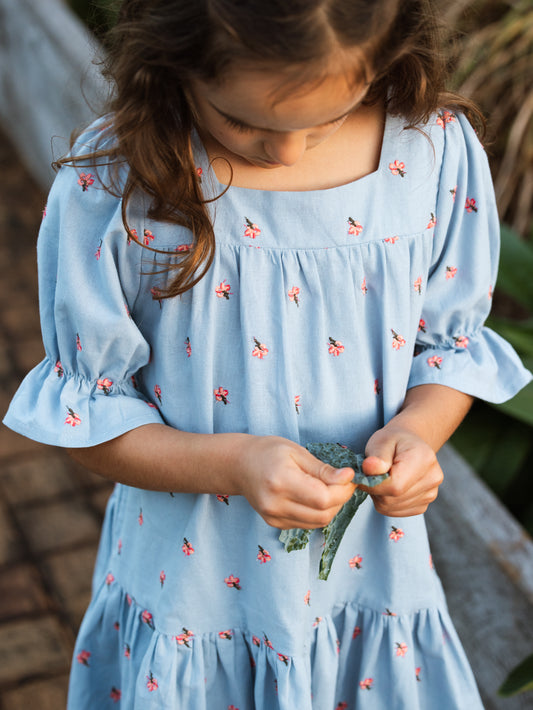 Young girl in a light blue dress with floral patterns outdoors.